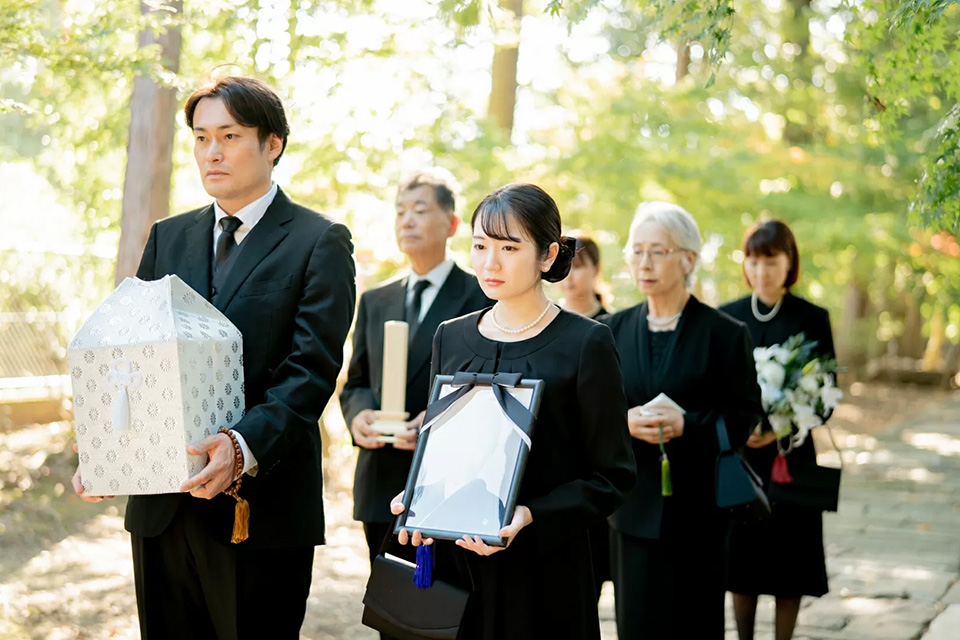 町田市の葬儀社であるファミリー福祉セレモニーの家族葬プランを象徴する、遺骨と遺影を抱えた家族のお見送り風景